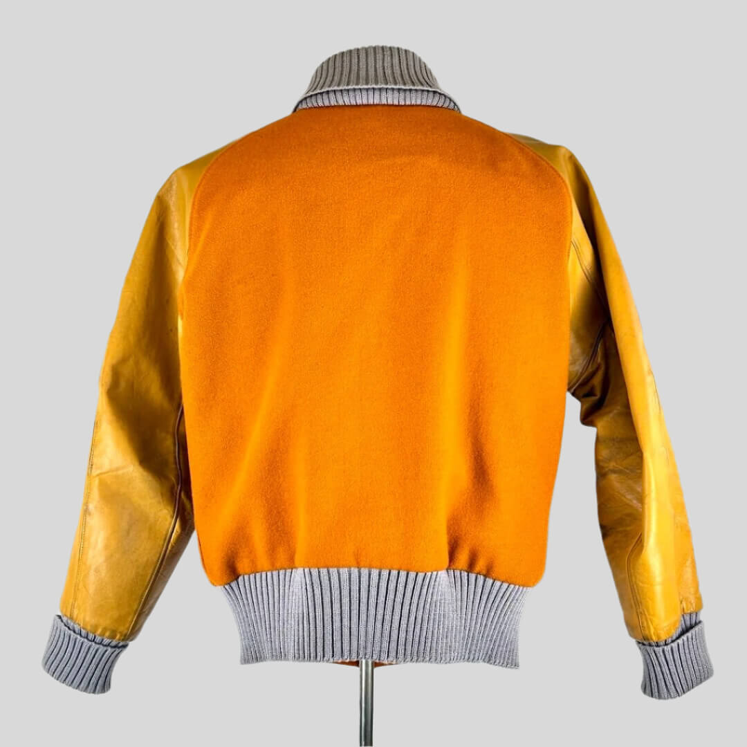 back view of orange varsity jacket with lighter orange leather sleeves, ribbed grey collar, cuffs and waistband. 