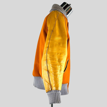 side view of orange varsity jacket with lighter orange leather sleeves, ribbed grey collar, cuffs and waistband.
