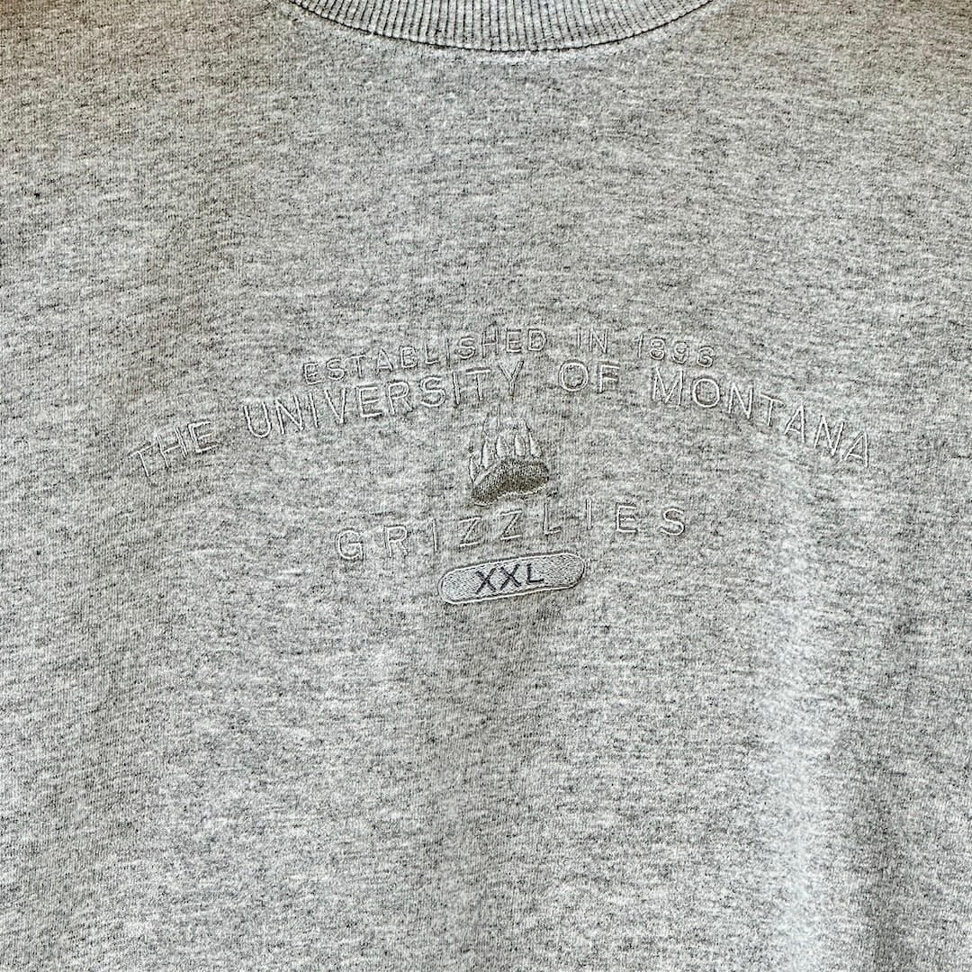 Close up of design on front embroidered in silver thread on heather grey sweater. School name above bear paw logo.