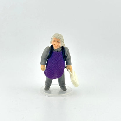 Alien action figure in gray outfit and purple apron holding white briefcase against white background.