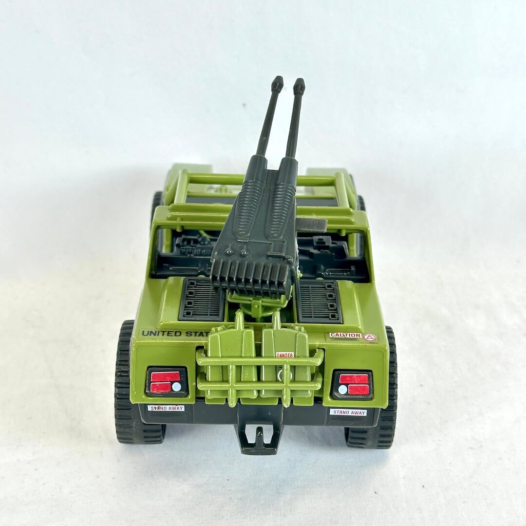 An olive green toy military vehicle with a gray twin-barrel weapon mounted on the back, displayed against a white background.