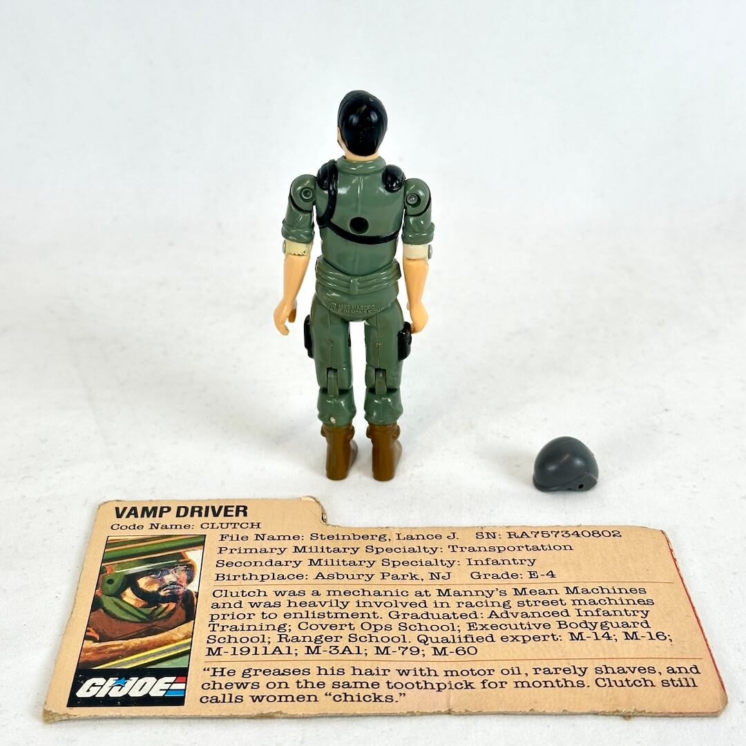 A vintage GI Joe action figure standing by a printed card and toy helmet. 