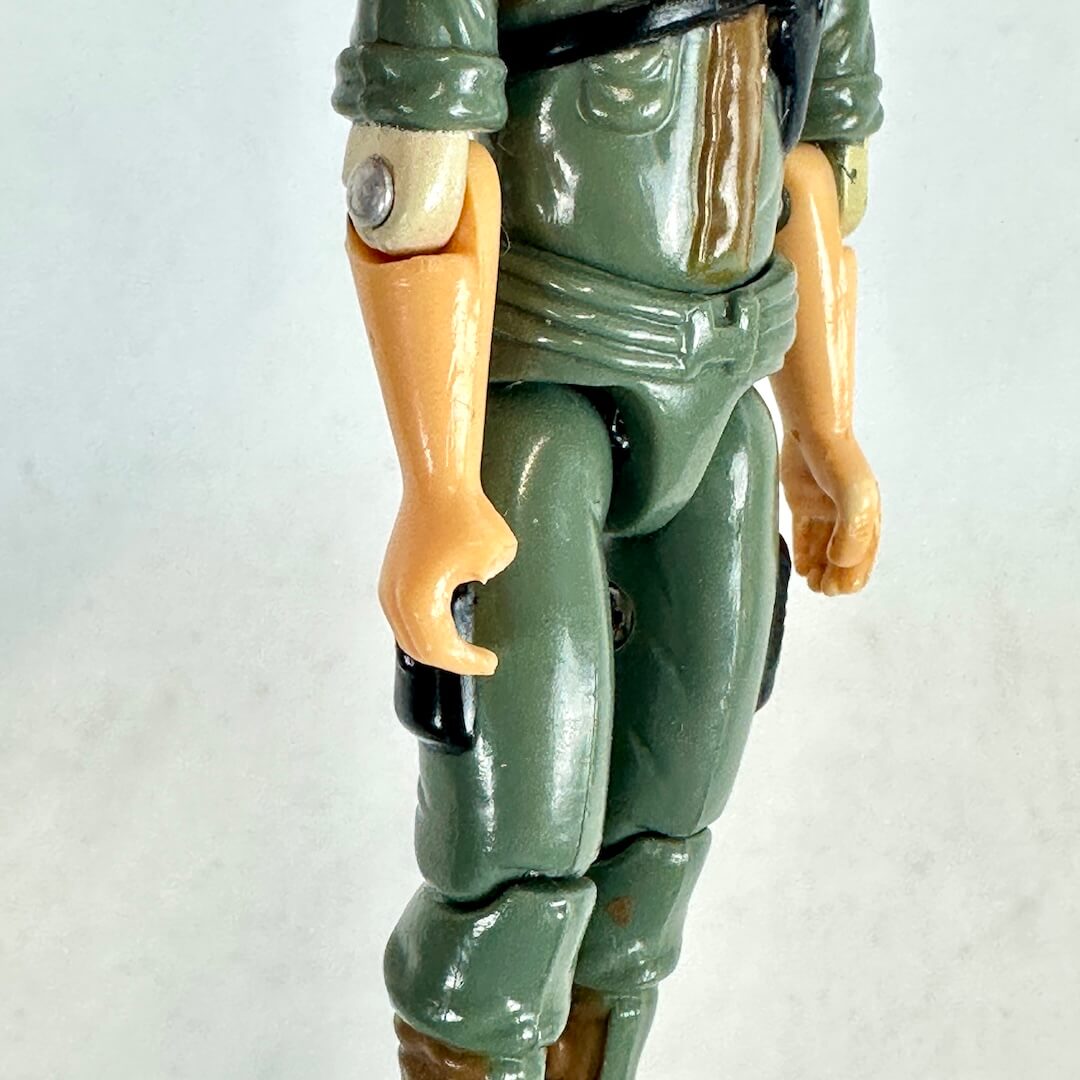 Close-up of a vintage plastic action figure torso and upper legs, painted in olive green with tan skin.