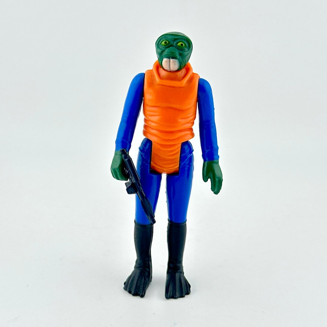 Action figure of alien in blue suit and orange shirt with weapon on white background.