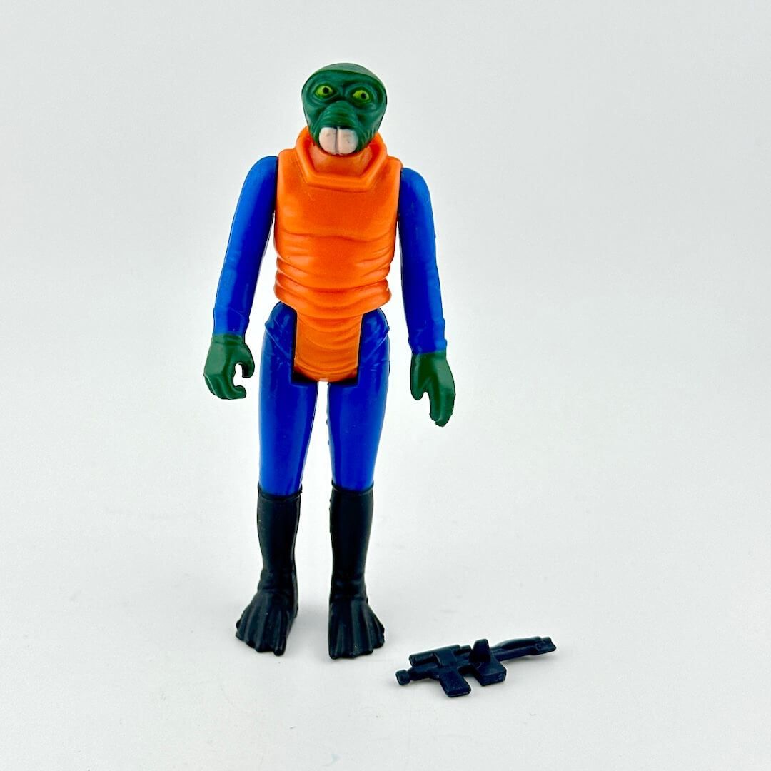 Action figure of alien in blue suit and orange shirt with weapon on white background.