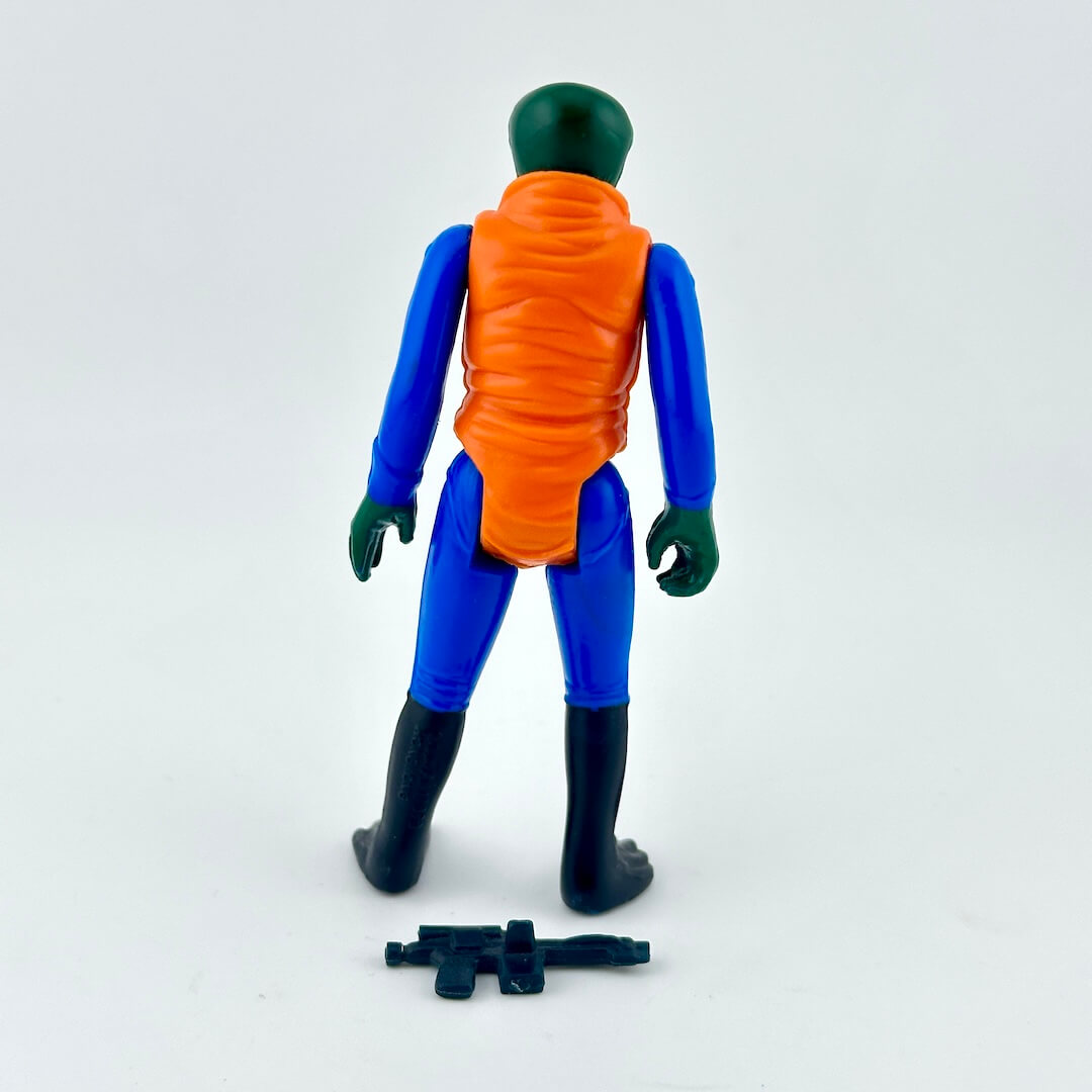 A vintage plastic action figure shown from the back, featuring a green head and hands, a blue body, and an orange vest. 
