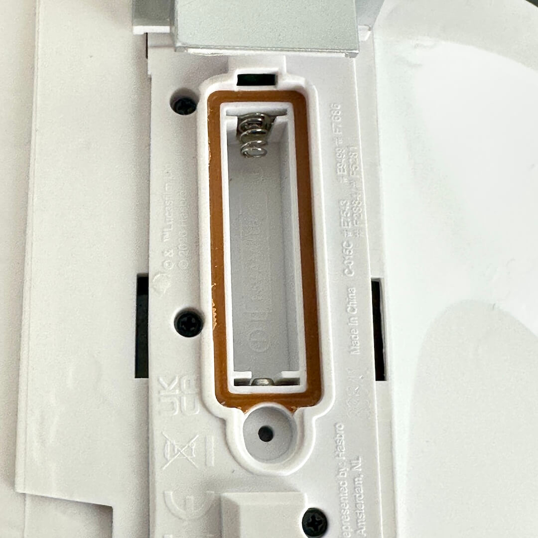 Close-up of a white plastic battery compartment or battery holder with a gold-colored inner tray and visible battery spring.