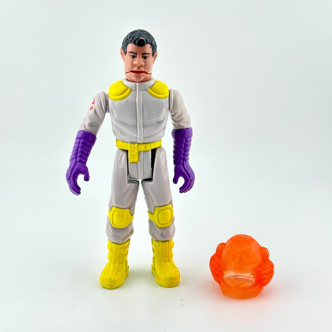 Toy figure in space suit with purple gloves and yellow boots, next to an orange toy.
