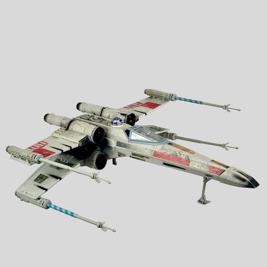 A detailed model of a Star Wars X-wing Starfighter, featuring weathered gray and white paint with red markings.