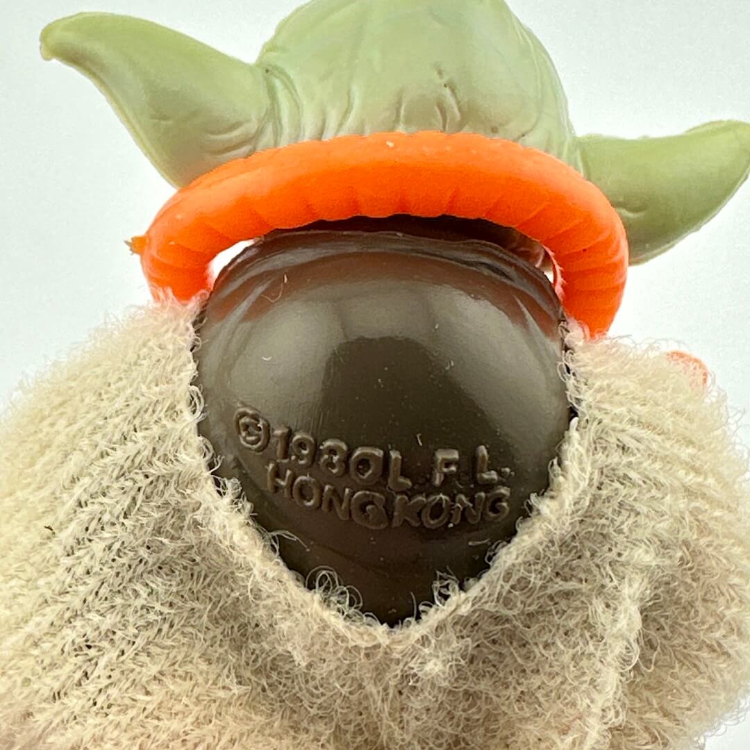 Close-up of a Yoda-like figure with an orange band around its head, featuring a visible brand logo.