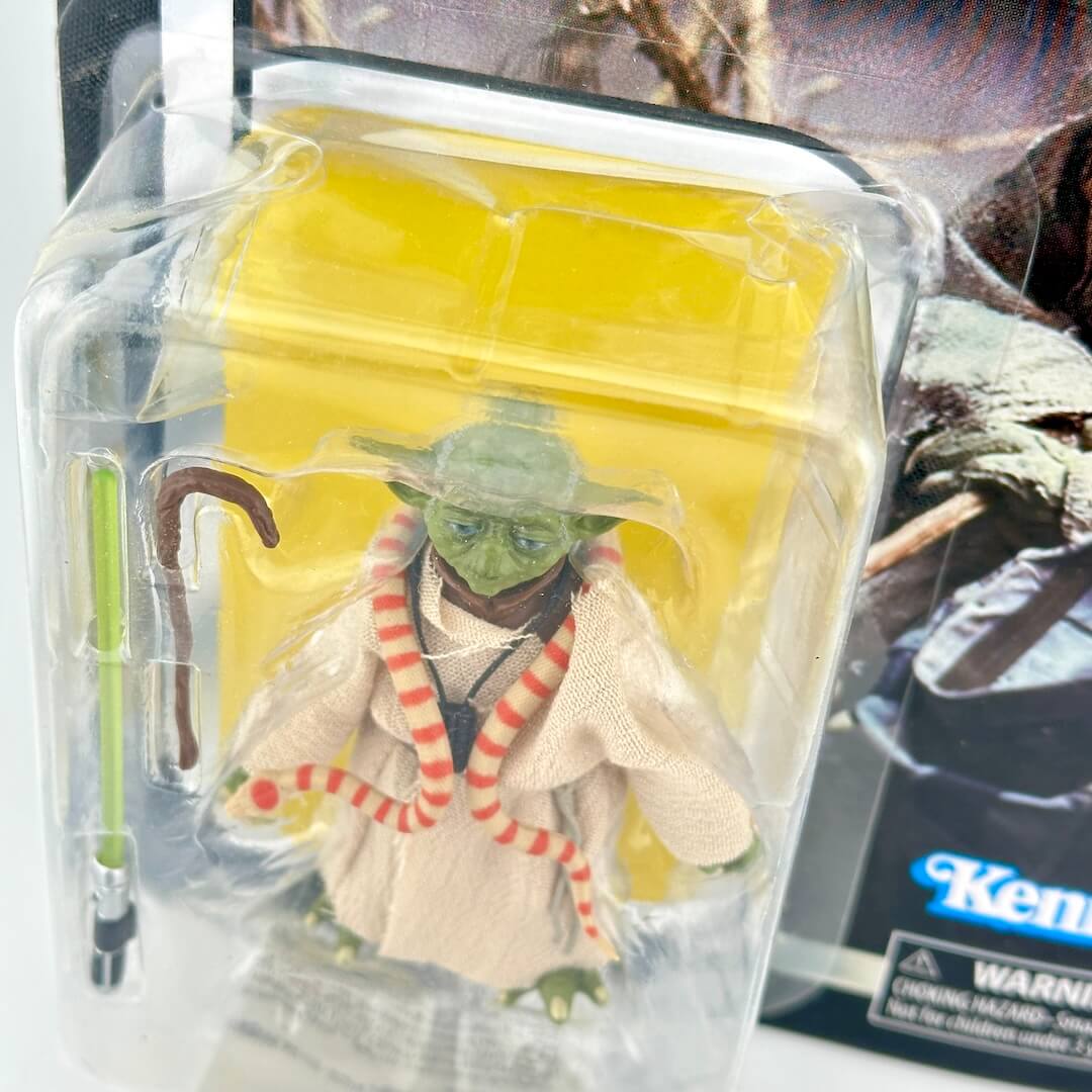 Action figure of Yoda from Star Wars, shown in its original blister packaging with a green lightsaber accessory.