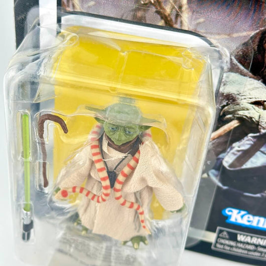 Action figure of Yoda from Star Wars, shown in its original blister packaging with a green lightsaber accessory.