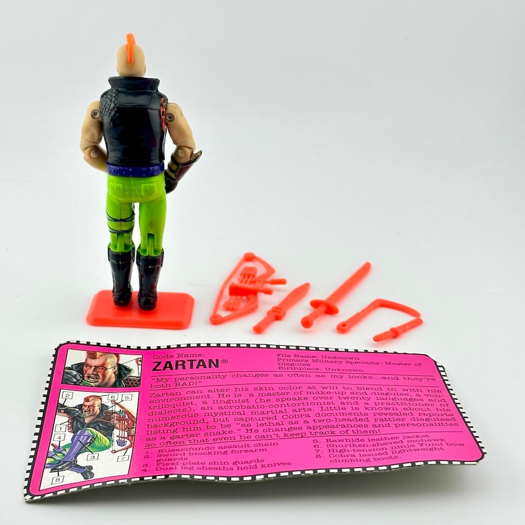 Toy figure of Zartan with accessories and character card on a white background